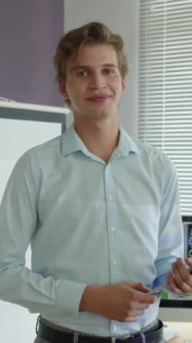 Kafkas erkek öğretmenin elinde ders planı tutarken ve bilişim dersinde kameraya gülümserken dikey portresi