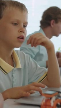 Sınıfın masasındaki kablosuz bilgisayarda internetten iş yapan iki ırklı öğrencilerin dikey görüntüsü.