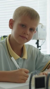 İlkokul yazı sınavındaki pozitif çocuğun dikey portresi ve kameraya bakışı