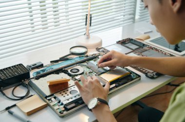 İşyerinde oturan tamirci atölyedeki aletlerle dizüstü bilgisayarı tamir ediyor.