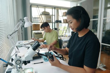 İş yerinde arka planda çalışan meslektaşı ile drone tamir eden genç bir kadın.