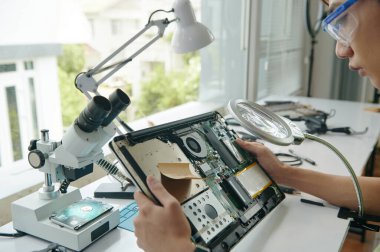 İşyerinde oturan teknisyenlerin yakın çekimleri ve dizüstü bilgisayarın detaylarını incelemeleri.