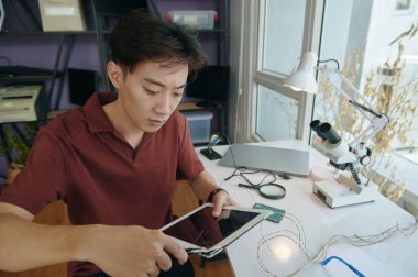 Genç efendi atölyede oturuyor ve tablet ekranını onarıyor.