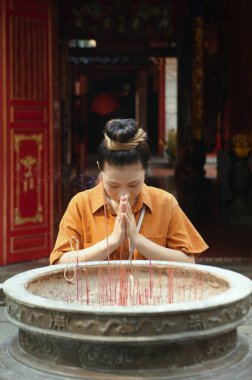 Asyalı kadın aroma çubuklarıyla büyük bardağın yanında durup dua ediyor.