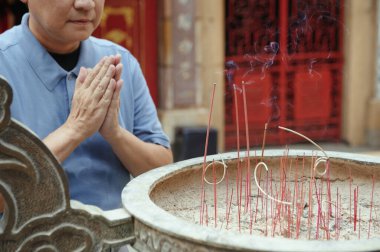 Asyalı adam tapınağın dışında aroma çubuklarıyla Kase 'nin yanında dua ediyor.