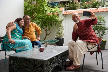 Eski arkadaşlar terasta vakit geçirirken cep telefonuyla selfie portresi yapıyorlar.