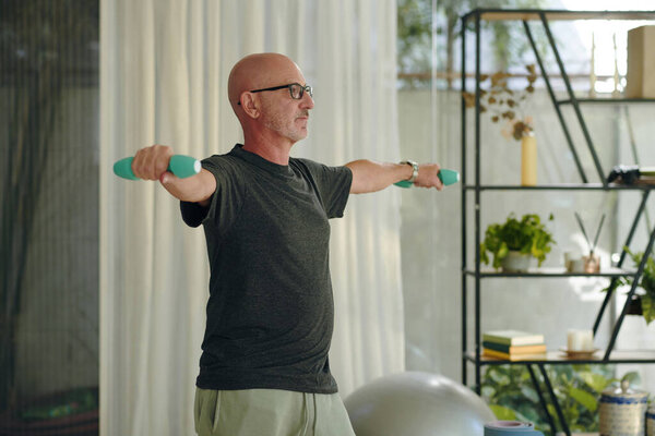 Elderly man lifting dumbbells in a home setting with indoor plants in background, staying fit and healthy by exercising indoors