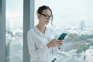 Ofis koridorunda dururken cep telefonuna mesaj atan genç bir iş kadını.