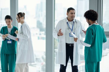 Doktorlar ve hemşireler hastane koridorunda dururken çalışma saatlerini tartışıyor.