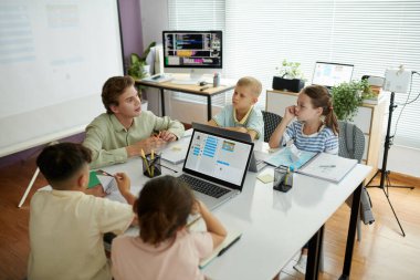 İnteraktif derse katılan çocuklardan oluşan bir grup modern sınıf ortamında dizüstü bilgisayarlar ve eğitim araçlarıyla donatılmış öğretmenler tarafından eğitilmektedir.