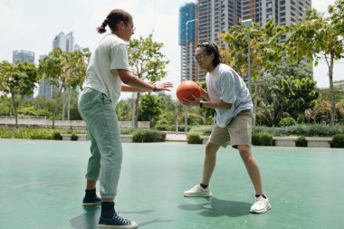 Yeşillik ve modern binalarla çevrili açık havada basketbol oynayan iki kişi.