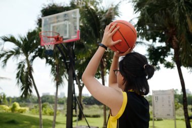 Yeşillik ve yüksek palmiye ağaçlarıyla çevrili açık alanda basket oynamaya hazırlanan biri.