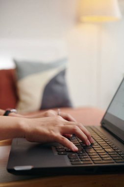 Yastıklarla ve arka planda sıcak aydınlatmayla rahat bir atmosfer yaratarak rahat bir evde otururken dizüstü bilgisayarın klavyesinde yazan kişi