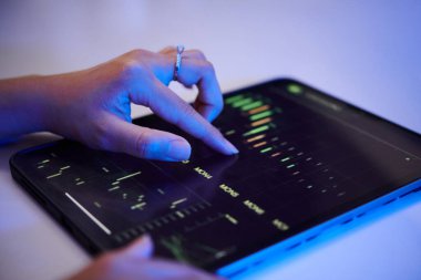 Mali grafikleri ve grafikleri loş aydınlatılmış bir ortamda analiz etmek, dijital etkileşimi ve modern teknoloji eğilimlerini vurgulamak için bir tablet aygıtı kullanan el.
