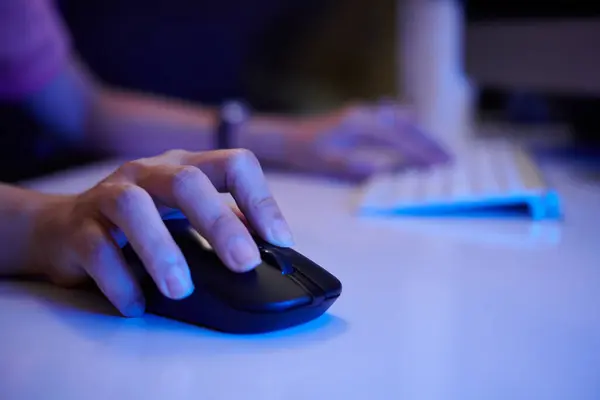 Stock image Person using black wireless mouse while typing on keyboard on blurry white table. Showing only hands, environment focused on technology and concentration