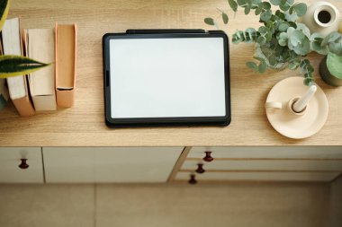 Odadaki kitapların arasında, çekmecenin üzerinde duran tablet bilgisayarının üst görünümü