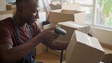 Orta boy siyah erkek tavlama noktası yöneticisi karton kutularda tarayıcı ve masa başı paketleri kullanıyor.