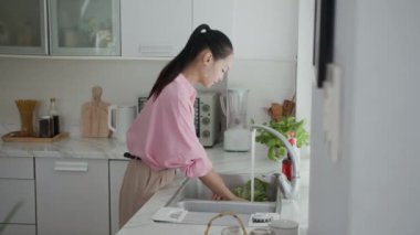 Mutfak lavabosunda sebze ve yeşillik yıkayan Asyalı bir kadın.