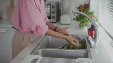 Anonim bir kadının evde yemek pişirirken mutfak lavabosunda sebze temizlemesi.