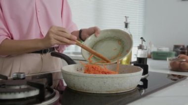 Anonim bir kadının evde öğle yemeği hazırlarken tavada havuç pişirirken görüntüsü.