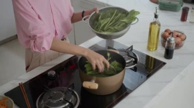 Mutfakta salata pişirirken yeşil yaprakları kaynatan isimsiz bir kadının görüntüsü.