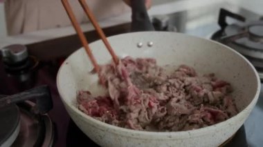 Akşam yemeği için tavada et pişiren tanınmayan kadının ellerini kapatın.