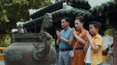 Asyalı ailenin kutsal tapınağı ziyaret ederken eğilip namaz kıldığı düşük açılı bir manzara.