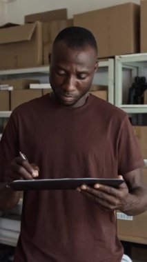 Afro-Amerikan depo müdürünün dikey portresi teslimat belgesini dolduruyor ve kameraya bakıyor