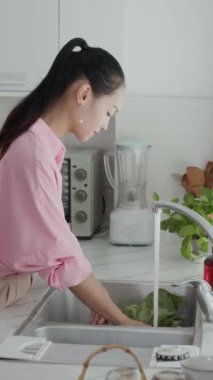 Asya kökenli bir kadın zoomer 'ın dikey yan görüntüsü lavaboda sebze ve sebzeleri duruluyor.