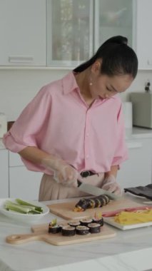 Ev mutfağında Kore kimbap 'ı dilimleyen Asyalı bir kadın zoomer' ın dikey görüntüsü.