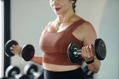 Spor salonunda spor yaparken dambılları kaldıran kaslı kadınların yakın çekimi.