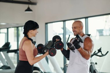 Spor salonunda birlikte antrenman yaparken dambıl kaldıran olgun bir çift.