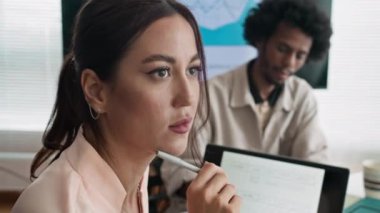 Genç beyaz kadın pazarlamacının iş kâğıdına notlar yazarken iş arkadaşlarıyla iş yerinde görüşürken aşağı eğilmesini.