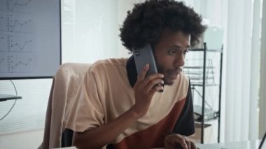 Genç girişimcinin ofis bilgisayarında çalışırken iş ortaklarıyla cep telefonuyla konuşurken elde çekilmiş bir fotoğrafı.