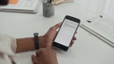 Tanımlanamayan yöneticinin ofis masasındaki akıllı telefondan e-posta okurken çekilmiş görüntüsü.