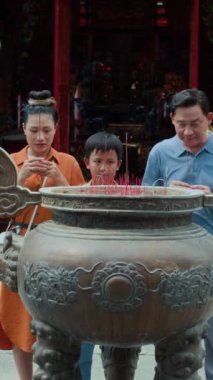 Asya kökenli bir ailenin dikey görüntüsü sunak başında açık havada yanan çubuklarla dua ederken.