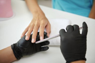 Profesyonel manikürcü müşterileri çivilerken müşteriler ellerini masaya koyup siyah eldiven kullanıyor ve temiz ve cilalı görünüm için hassasiyet kullanıyor.