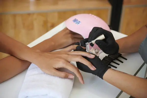 stock image Manicurist wearing black gloves carefully using nail file on clients nails during manicure session in nail salon with clean and organized work environment