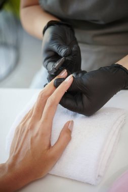 Siyah eldivenli teknisyenlerin hassas aletlerle tırnaklarını kestiği manikür seansı sırasında el ele tutuşun. Bakım sürecinde el havluya dayanır