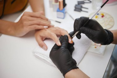 Müşterilere oje hizmeti veren profesyonel manikürcünün yakın plan görüntüsü. Temiz ve düzenli kuaför ortamında uzman el bakımı.