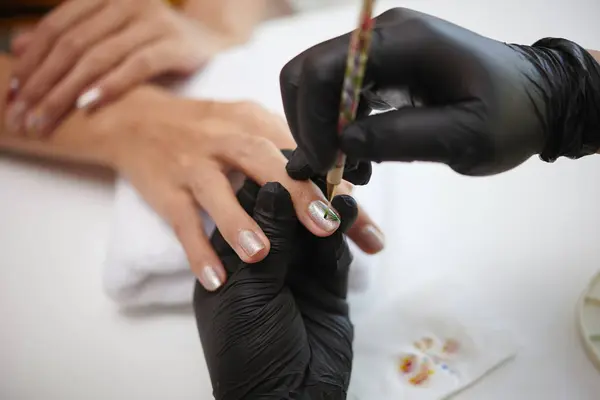 stock image Close-up of gloved professional applying metallic nail polish on womans hand, focusing on details of careful nail care work