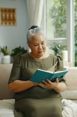 Büyükannem oturma odasında kanepede otururken ilginç bir kitap okuyor.