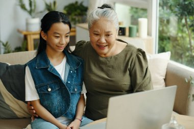 Büyükannem, torunuyla birlikte oturma odasında otururken dizüstü bilgisayarda video izliyor.