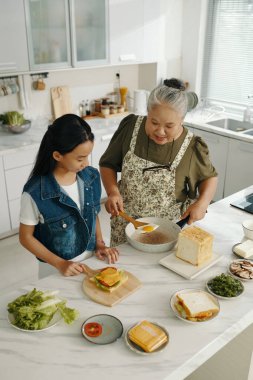 Büyükannesi, torunuyla birlikte mutfakta sandviç ve sahanda yumurta pişiriyor.
