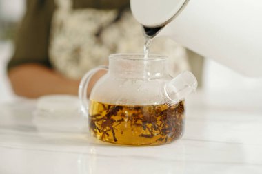 Ev hanımı kahvaltıda siyah çay yapmak için çaydanlığa sıcak su dolduruyor.