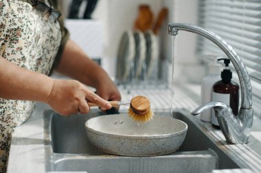 Ev hanımının mutfakta kirli tavayı temizlemek için fırça kullanması.