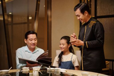 Garson misafirlerle konuşuyor ve restoranda sipariş veriyor.