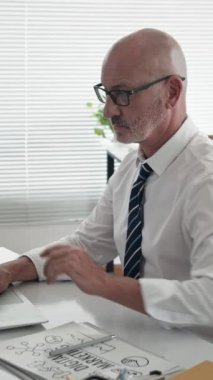 Ofiste dizüstü bilgisayarla çalışan orta yaşlı, kendine güvenen beyaz iş adamının dikey portresi.
