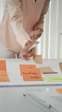 Ofiste iş planı üzerinde çalışırken isimsiz proje yöneticilerinin etiketleri kağıda yapıştırdığı dikey çekim