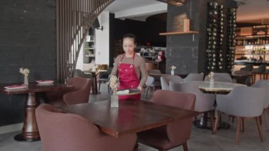 Sofistike bir restoranda kırmızı önlüklü genç Asyalı garsonun masaları silişi.
